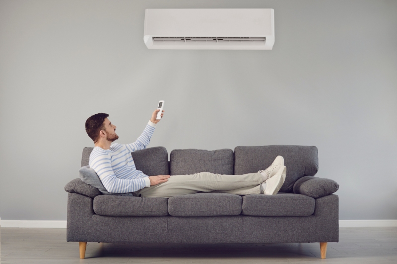 Homem usando controle remoto de ar-condicionado em sala climatizada